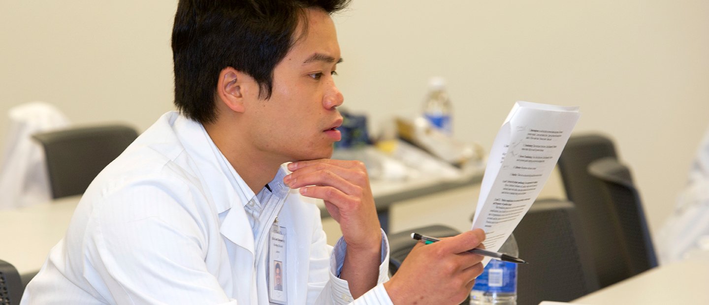 man in a white lab coat holding a pencil, looking over a form