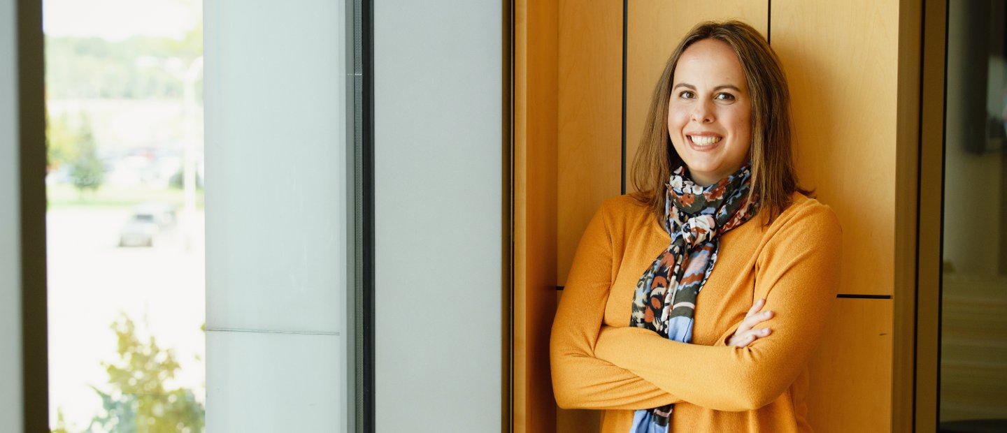 A woman standing in front of a window with her arms folded, smiling at the camera.