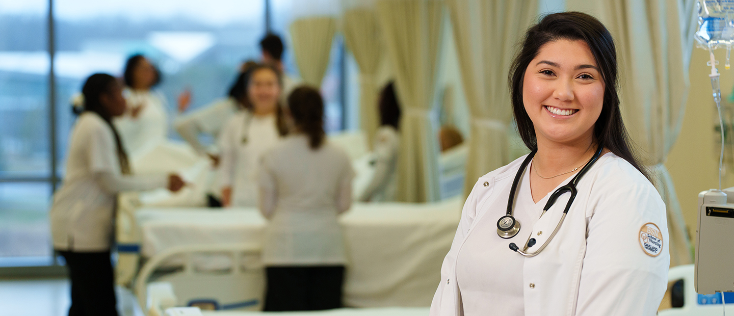 A nurse in a white lab coat, with a stethoscope around her neck, smiling at the camera.