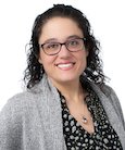 Headshot: Woman in dark top grey jacket with short brown hair and glasses smiling at camera.