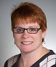 woman in a black and white shirt and glasses smiling at the camera