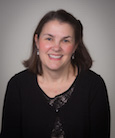 Headshot: Dark haired woman in dark top smiling at the camera.