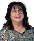 Headshot: Dark haired woman in paisley top and glasses smiling at the camera