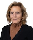 Headshot: Blonde woman in lt. brown turtleneck with black jacket smiling at camera