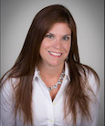 Headshot: dark haired woman in a white button down shirt smiling at the camera