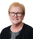 Headshot: Blonde woman with glasses in black top smiling at camera