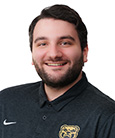 Headshot: Dark haired man in dark shirt and beard smiling at the camera