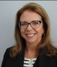 Headshot: woman in a black and white shirt, black jacket and glasses smiling at the camera