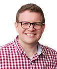 Headshot: Man in red and white with glasses smiling at camera