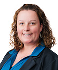 Headshot: Woman in Blue top and black jacket smiling at the camera