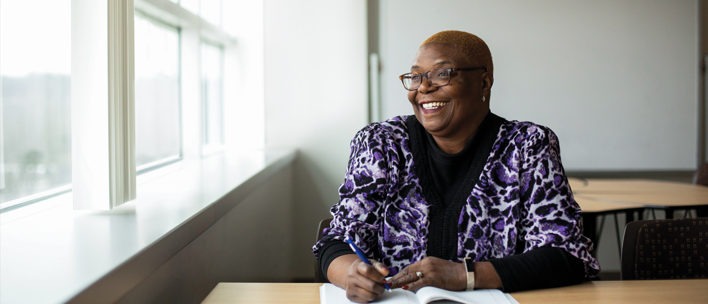 Photo of an african american woman sitting at a desk smiling out the window next to her