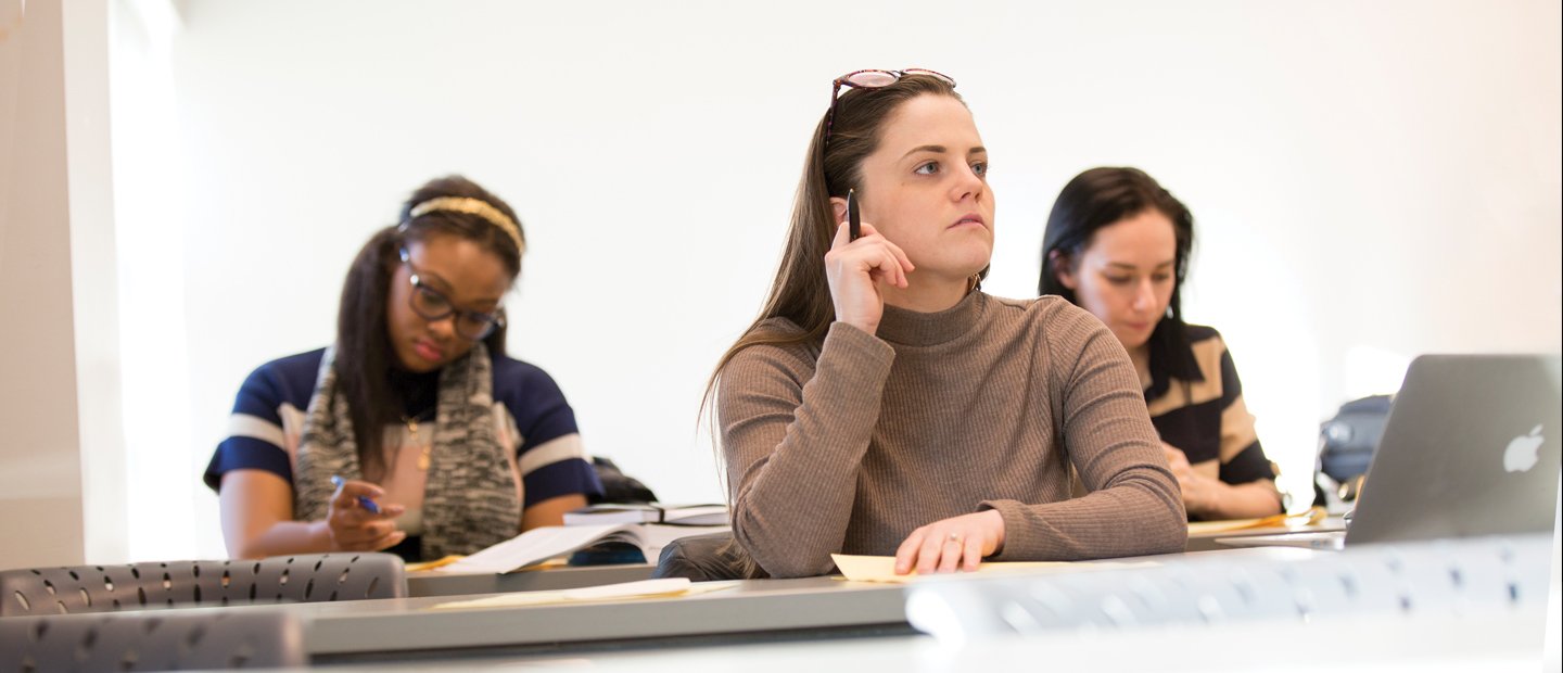 young women seated at desks in a classroom, looking to the front of the room