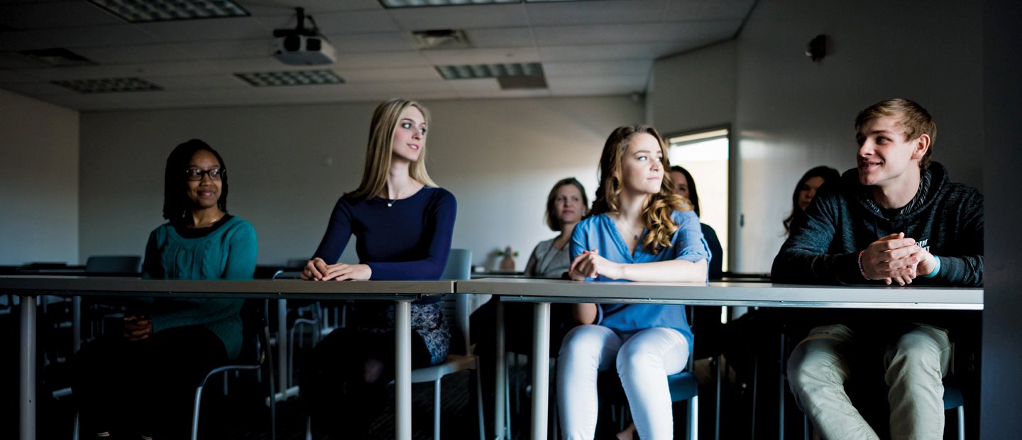 students seated at long tables in a dark classroom